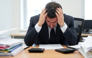 Professional experiencing workplace stress while sitting at an office desk with paperwork and documents.